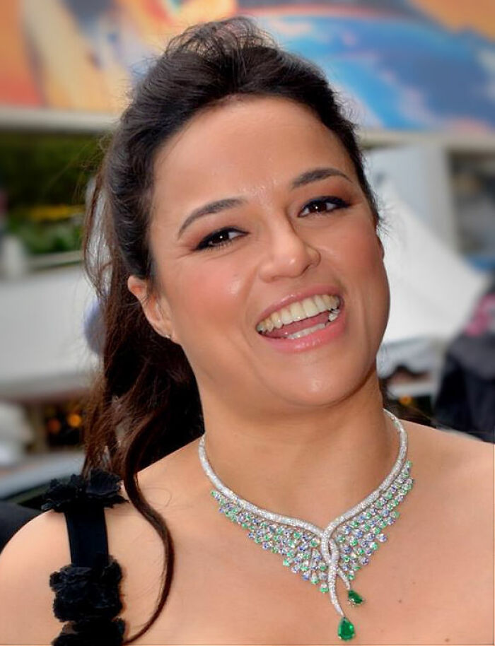 Michelle Rodriguez smiling at an event, wearing a beautiful diamond and emerald necklace, showcasing her career highlights.