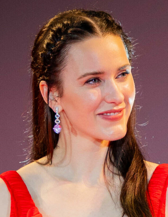Rachel Brosnahan smiling, wearing a red dress and drop earrings, highlighting her notable career.