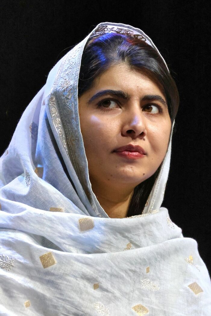 Malala Yousafzai, Nobel laureate and activist, wearing a light blue headscarf, looking up and to the right, against a dark background, highlighting her bio and career.