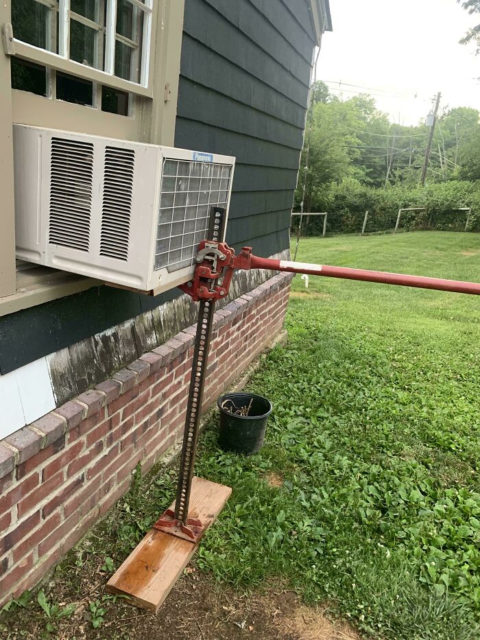 A car jack supporting an air conditioner in a window, illustrating people turning random junk into clever solutions.