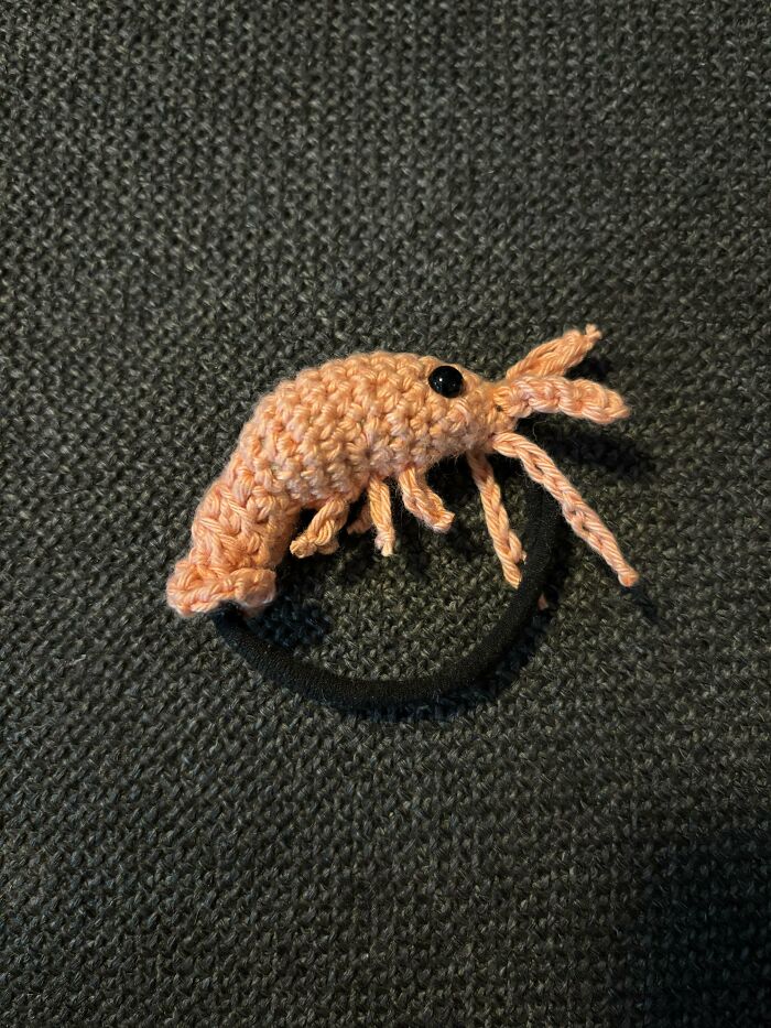 A close-up of a tiny, cute shrimp-shaped crochet hair tie, a useful DIY creation.