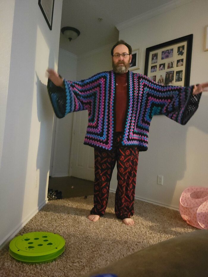 A man wearing a vibrant, multicolored crochet cardigan with large sleeves and black accents, a unique and useful DIY creation.