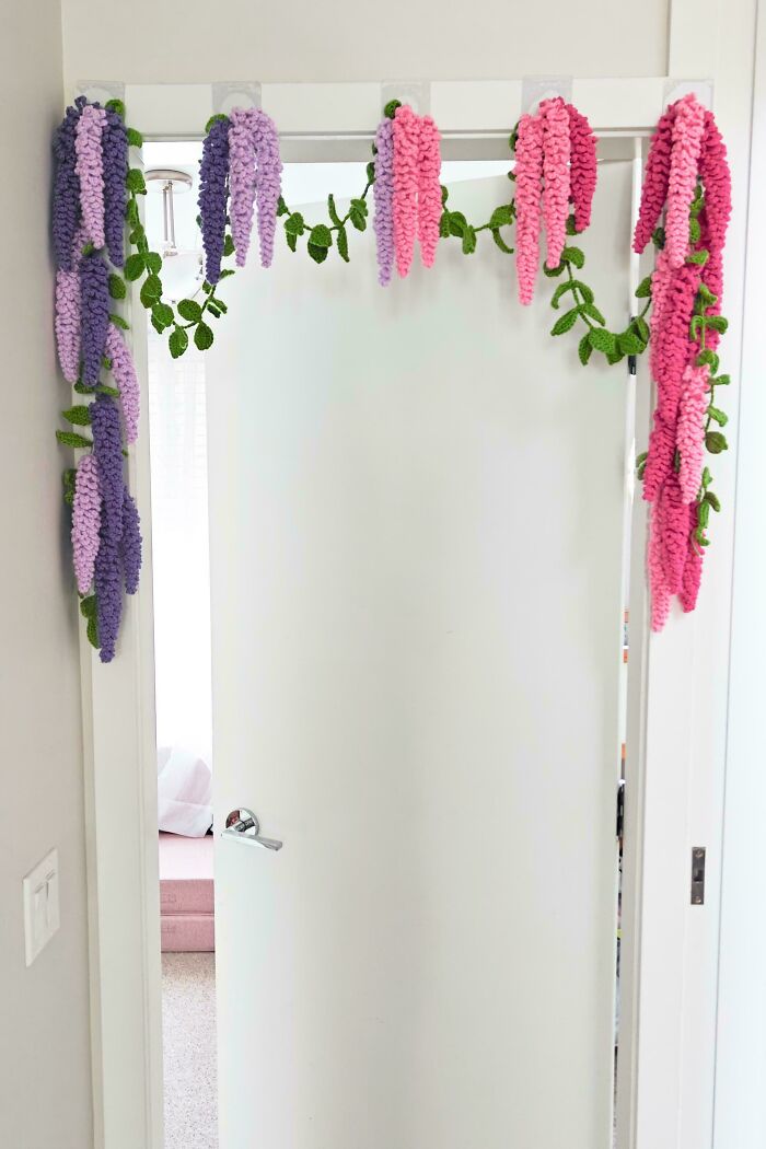 A vibrant crochet wisteria garland in pink, purple, and green hanging over a doorway, a decorative DIY creation.