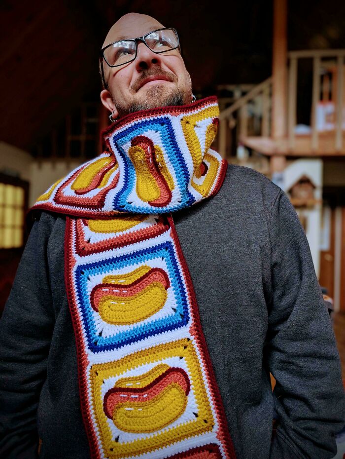 A man proudly wearing a fun, colorful crochet scarf with hot dog designs, a creative DIY creation.