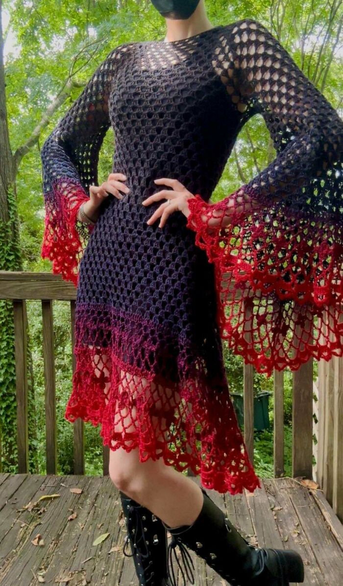 A person wearing a black and red crochet dress with wide sleeves, showing off a DIY creation.