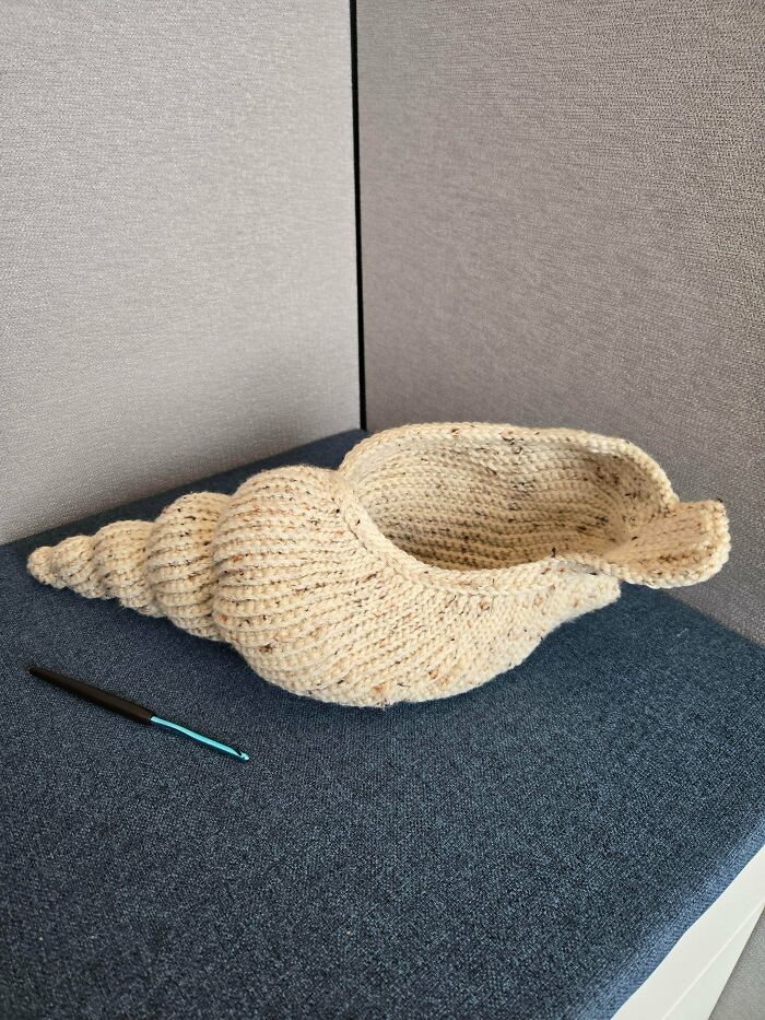 A crochet seashell basket, a useful DIY creation, with a crochet hook next to it.