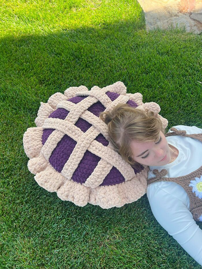 A person resting their head on a large, purple and beige crochet pie-shaped pillow, a DIY creation.