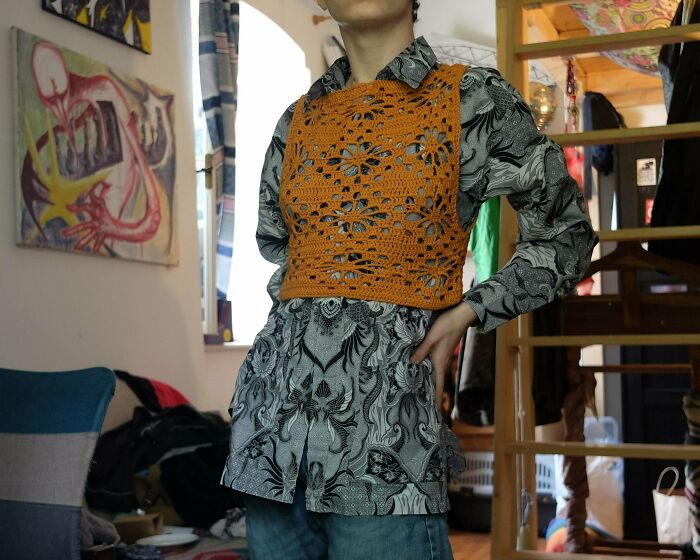 A person wearing a patterned shirt and a stylish orange DIY crochet vest, a useful crochet creation.