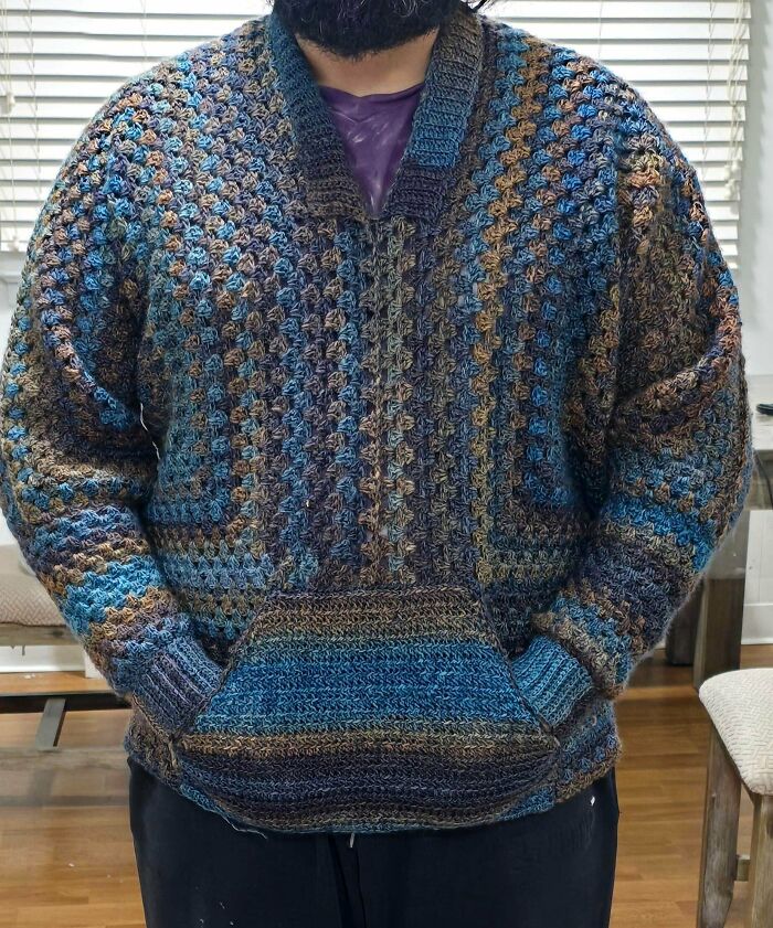 A man models a blue and brown crochet sweater, a useful DIY creation with a front pocket.