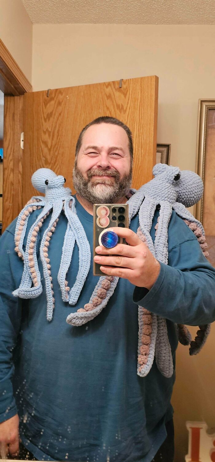 A man wearing two large DIY crochet octopus plushies on his shoulders, proudly displaying useful crochet creations.