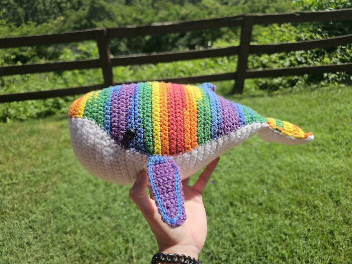 A hand holding a vibrant rainbow-striped crochet whale, a charming DIY creation.