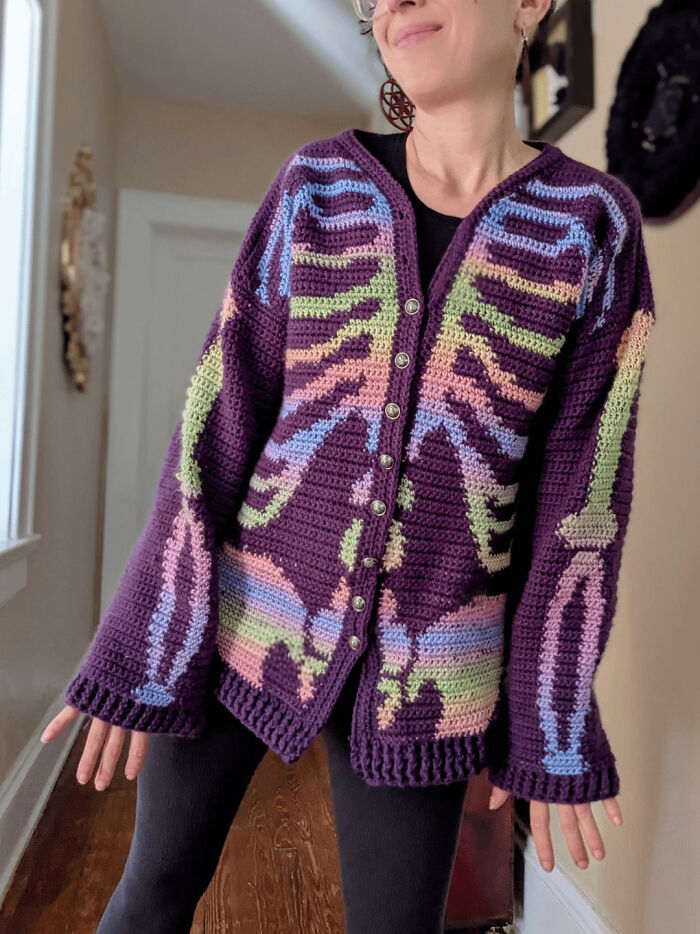 A woman modeling a dark purple crochet cardigan with a colorful skeleton design, a cool DIY creation.