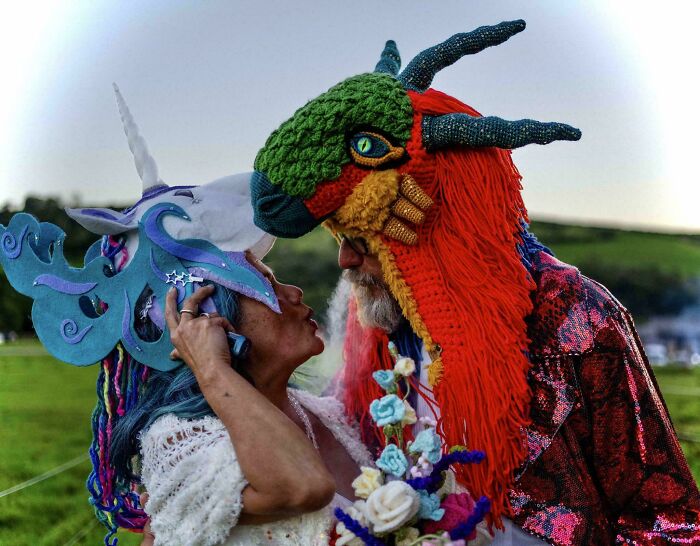 A couple wearing elaborate DIY crochet creations, a colorful dragon costume for him and a unicorn horn for her.