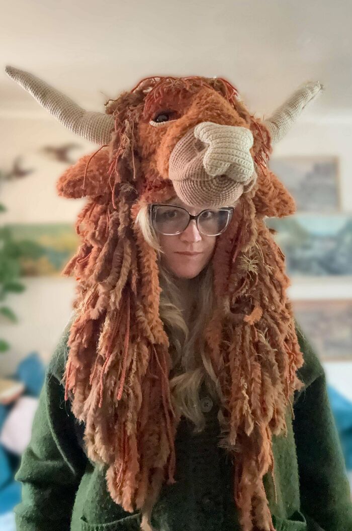 A woman wearing a creative crochet Highland cow hat, showcasing a unique DIY creation.