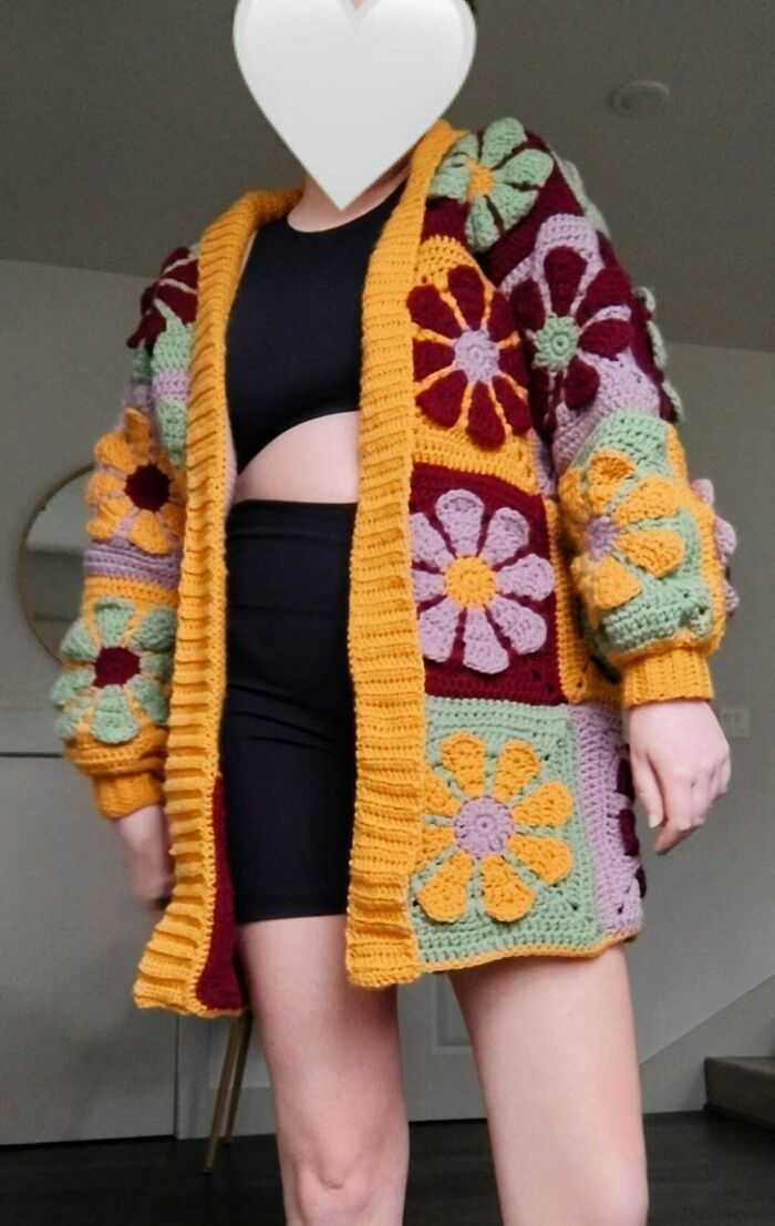 A person modeling a colorful DIY crochet cardigan with large floral appliques in various shades.