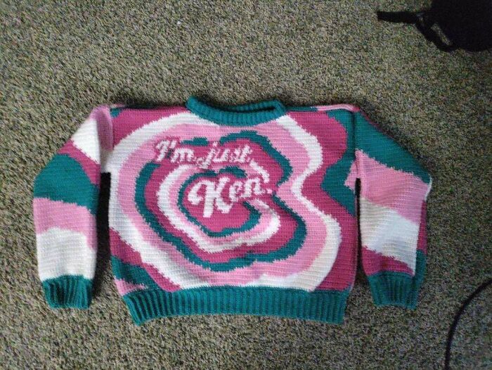 A pink, white, and teal DIY crochet sweater with the phrase 'I'm just Ken' in the center.