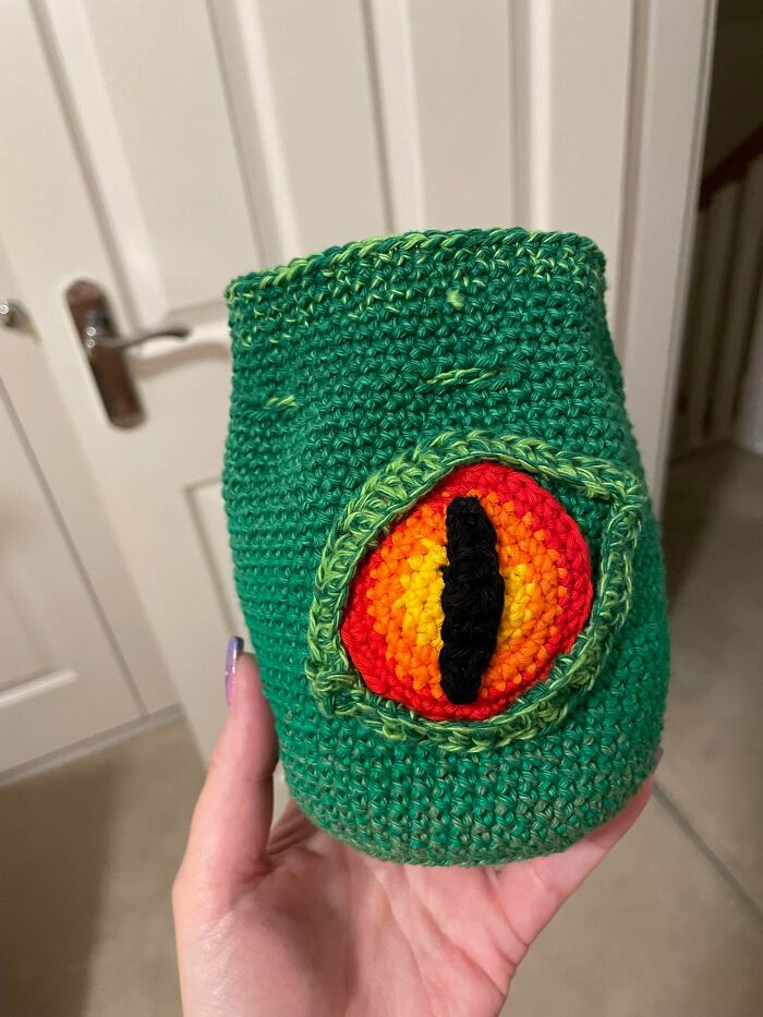 A hand holds a green DIY crochet bag with a vibrant dragon eye design, a creative and useful DIY crochet creation.