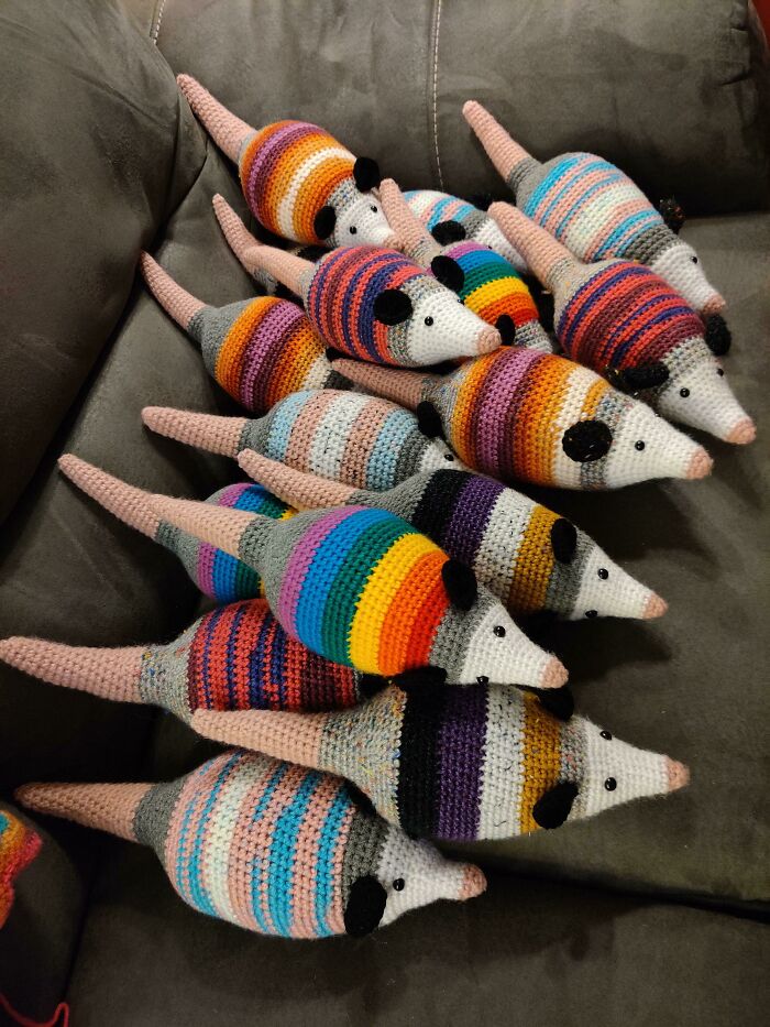 A collection of colorful striped opossum-shaped DIY crochet creations are piled on a couch, showcasing creative crochet creations.