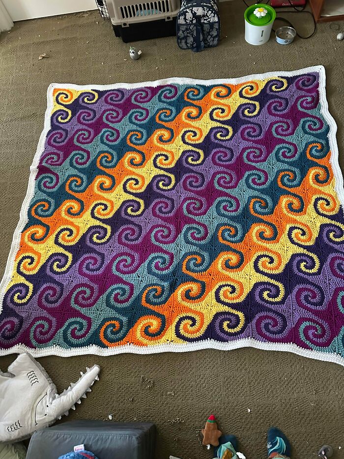 A large crochet blanket with a vibrant spiral pattern in yellow, orange, purple, and teal, a useful DIY creation.