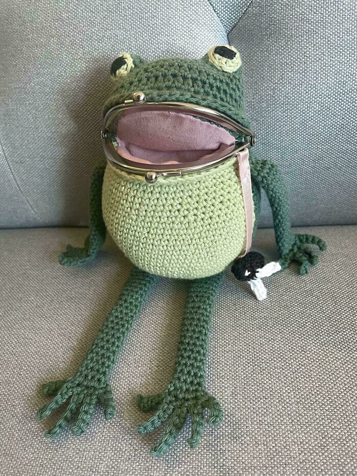 A DIY crochet frog-shaped coin purse sits on a grey couch, highlighting useful crochet creations.