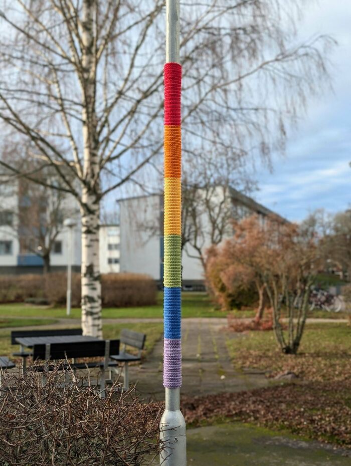 A rainbow-colored crochet yarn b**b on a pole in a park, demonstrating useful DIY crochet creations.
