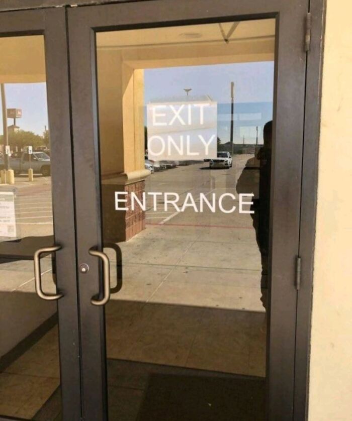 A glass door with conflicting signs: EXIT ONLY and ENTRANCE, reflecting a cultural decline into idiocy.