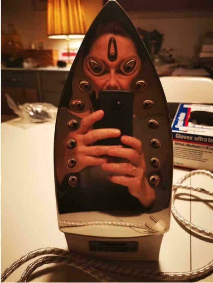A distorted reflection of a person with multiple eyes in an iron, forming a creepy image.