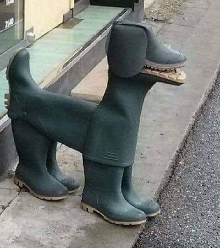 A dog sculpture made from several green rubber boots, standing on a sidewalk, a creepy image for nightmare fuel.