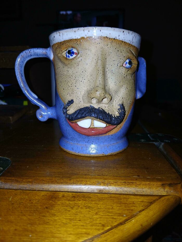 A ceramic mug shaped like a face with a blue mustache, googly eyes, and a wide, red-lipped grin. This creepy image is nightmare fuel.