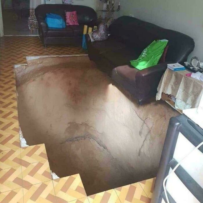 A large sinkhole has opened in the middle of a living room floor, revealing a deep, dark abyss. This creepy image is truly nightmare fuel.