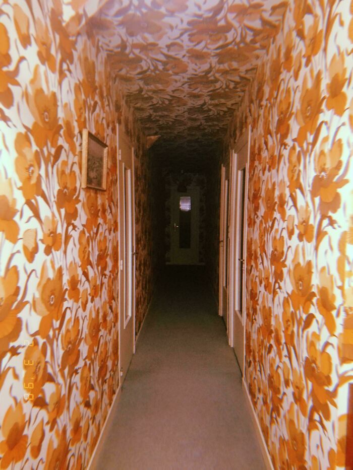 A long, dark hallway with vintage orange floral wallpaper, creating a creepy and unsettling scene, nightmare fuel.