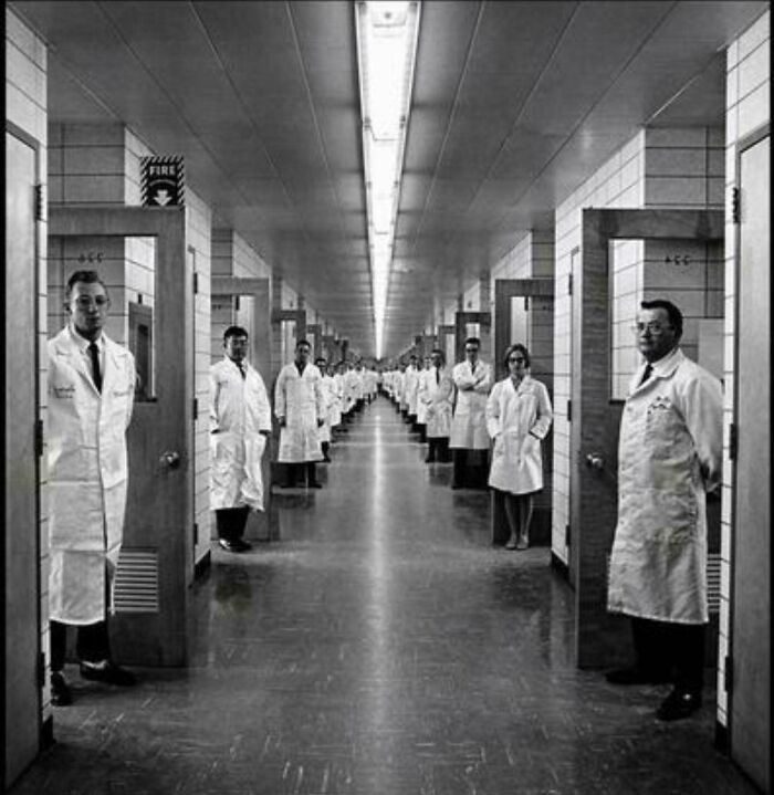 A long hallway with numerous doctors in lab coats standing in doorways, a creepy image that evokes nightmare fuel.