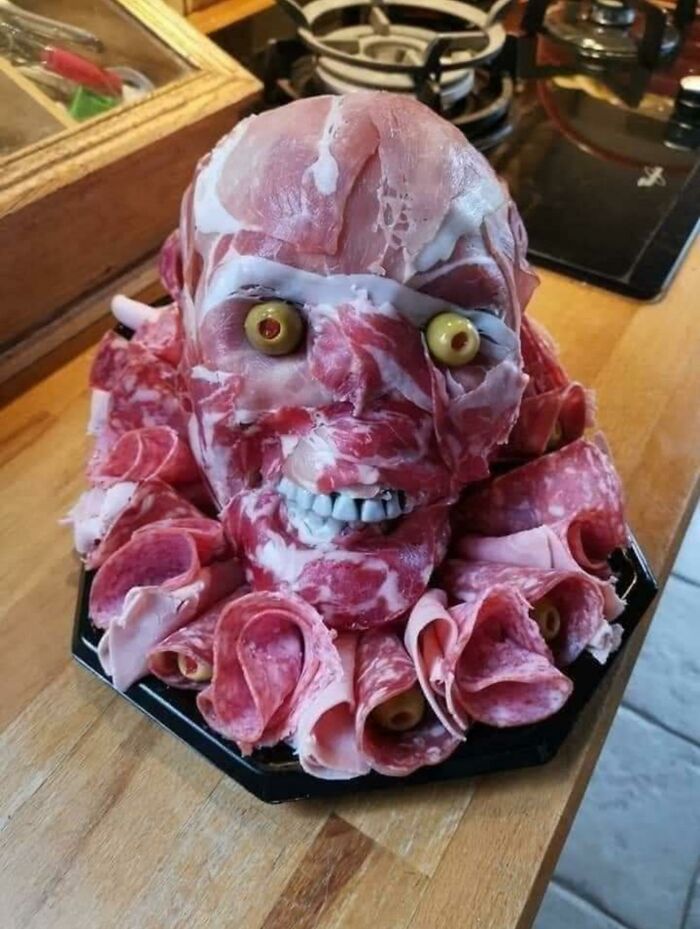 A head-shaped meat platter with olives for eyes and teeth, a creative yet potentially disgusting food presentation.