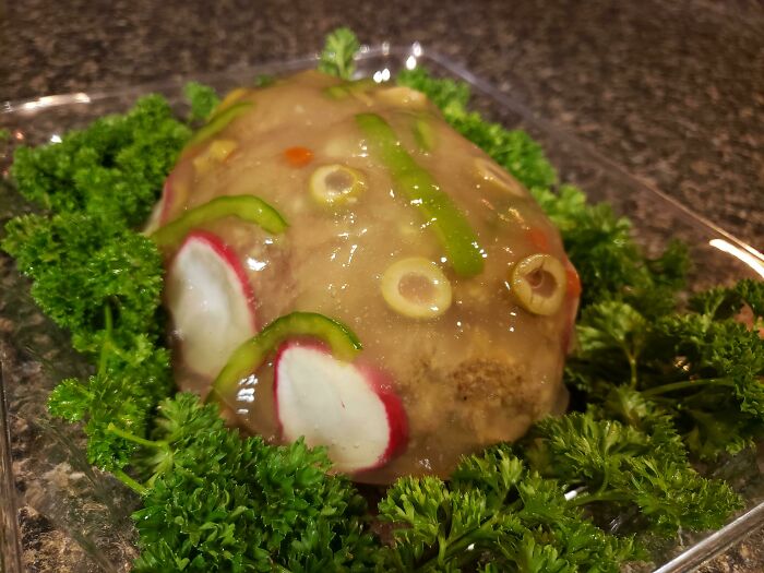 A gelatinous mold with vegetables like olives and radishes, showcased as disgusting food.