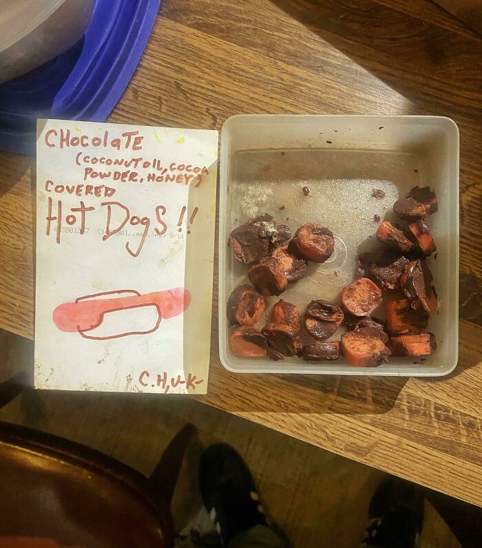 Chocolate-covered hot dogs with a handwritten sign, a bizarre and potentially disgusting food combination.