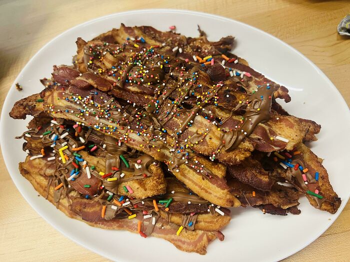 A plate piled high with disgusting food: crispy bacon strips covered in chocolate drizzle and colorful sprinkles.