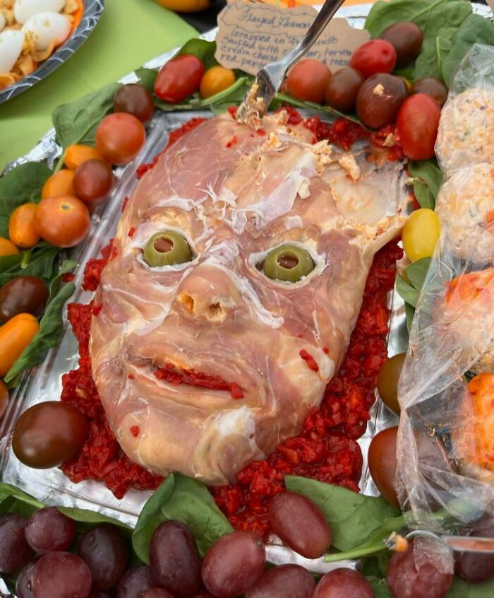 A truly disgusting food creation shaped like a severed head, made of meat, with olive eyes and tomato accents.