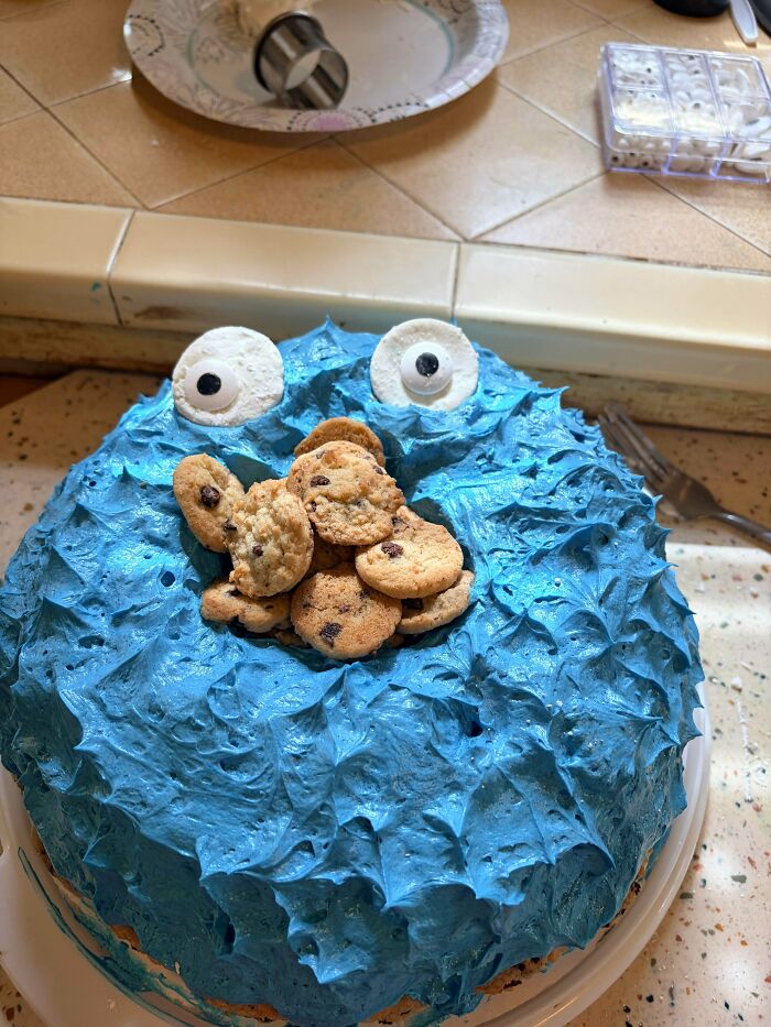 A creative baker's delicious cake designed to look like a blue monster with big eyes and chocolate chip cookies.
