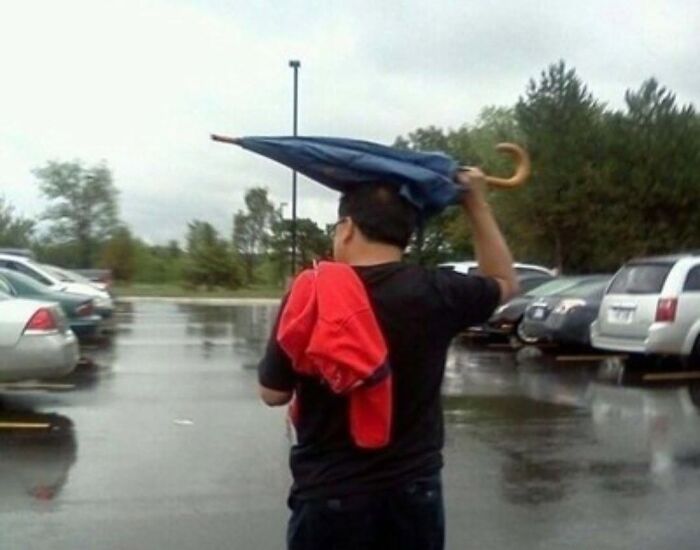 A person holding an inverted umbrella on their head in the rain, a ridiculous post showing cultural decline.