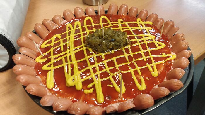 A large dish covered in ketchup, mustard, relish, and surrounded by mini hot dogs, a truly disgusting food item.