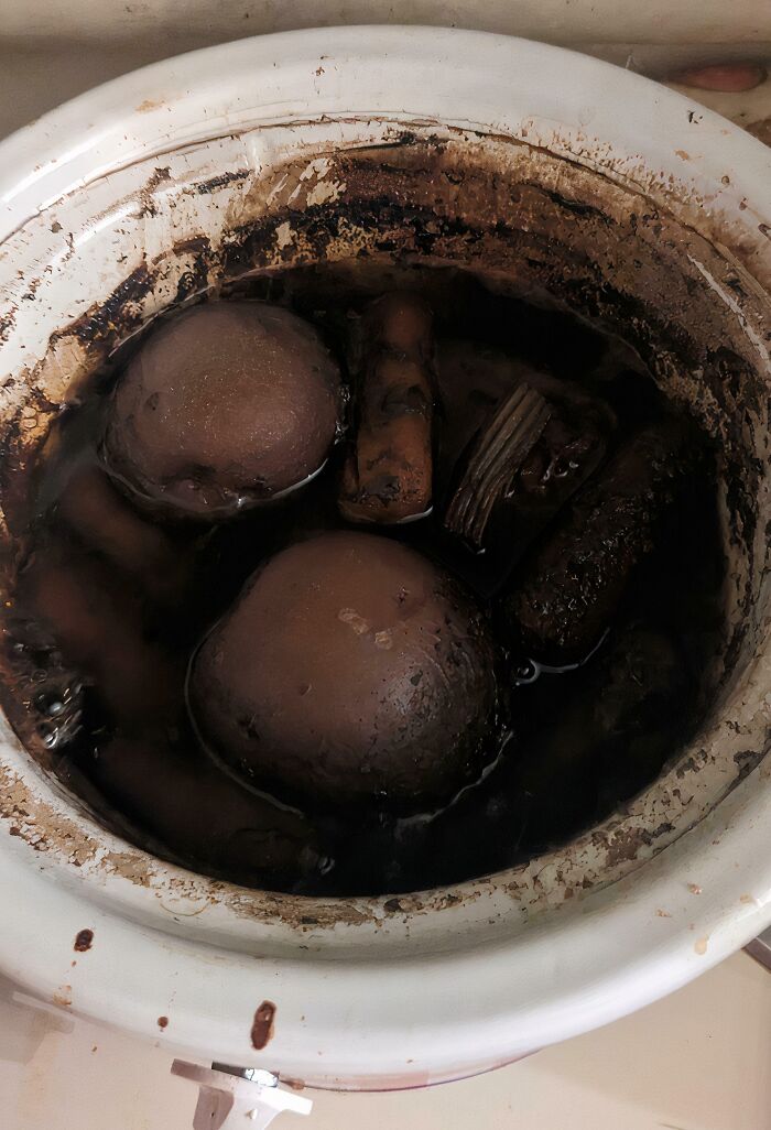 A slow cooker filled with dark, murky liquid and several unidentifiable, dark, disgusting food items.