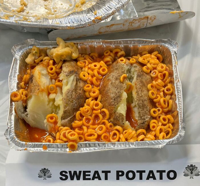 A baked potato dish with spaghetti rings and a sign calling it SWEAT POTATO, a truly disgusting food.