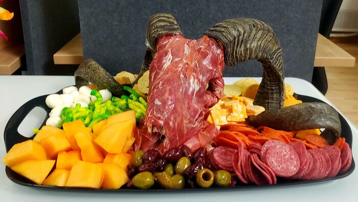 A charcuterie board featuring various meats, cheeses, and fruit, presented with a ram's head, making for a disgusting food display.