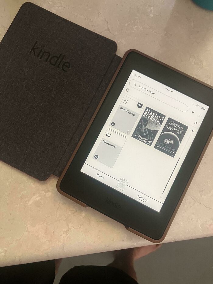 A Kindle e-reader displaying books, reflecting on insulting consumerism with a 400% price difference in digital vs. physical media.