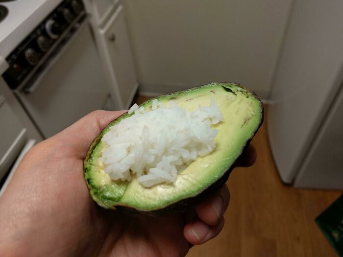 A hand holding a half avocado filled with white rice, a prime example of stupid vegan food.