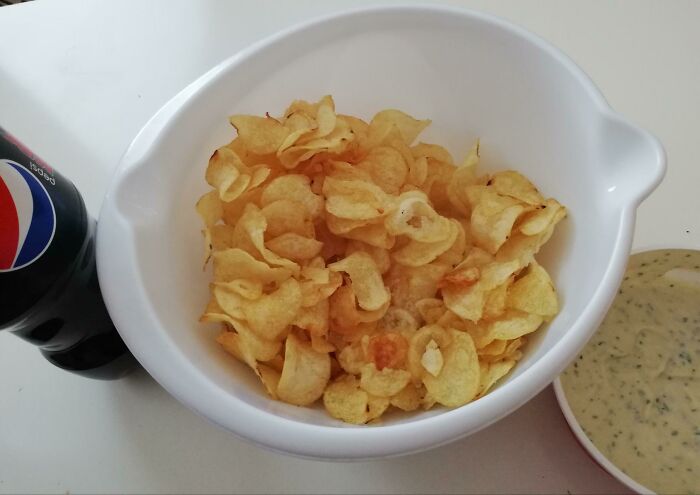 A bowl of potato chips next to a bottle of soda and a dip, highlighting stupid vegan food choices.