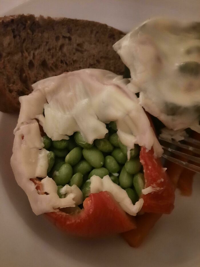 Red bell pepper stuffed with edamame and topped with cabbage, beside a slice of dark bread, portraying stupid vegan food.