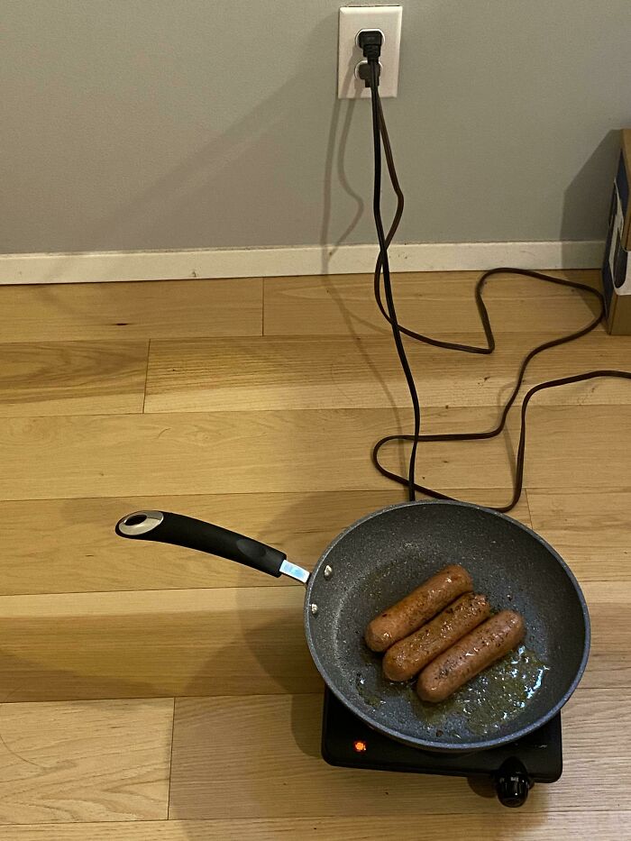 Three sausages cook in a frying pan on a portable burner, plugged into a wall outlet, representing stupid vegan food.