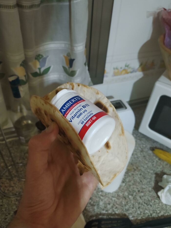 A hand holds a tortilla containing a bottle of Vitamin B12, a strange example of stupid vegan food.