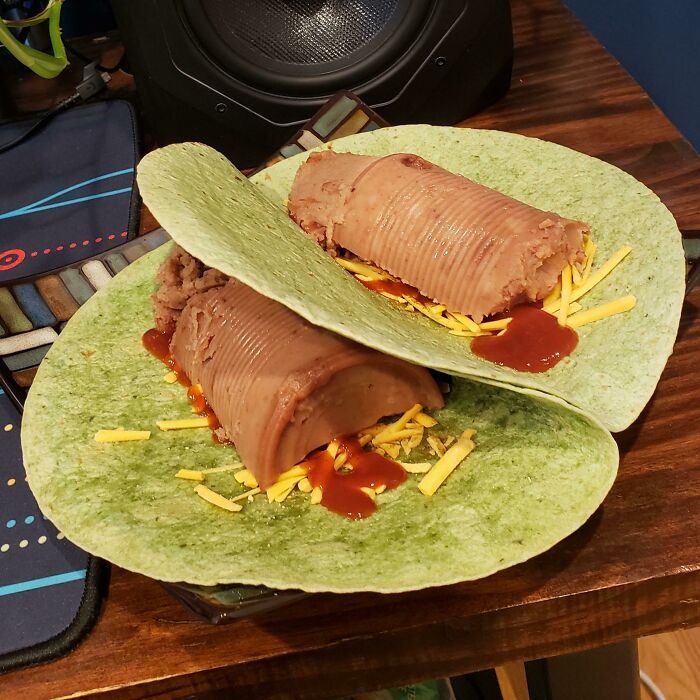 Two burritos made with green tortillas, a log of brown refried beans, cheese, and hot sauce, representing stupid vegan food.